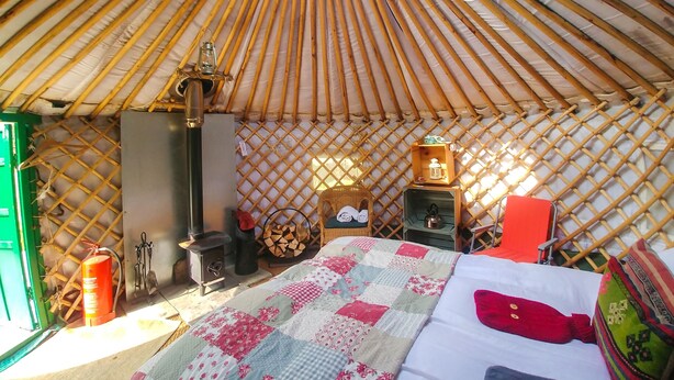 A yurt interior with a bed, a small heater, a lantern, and a firewood storage area. - Bamff Ecotourism (Blairgowrie)