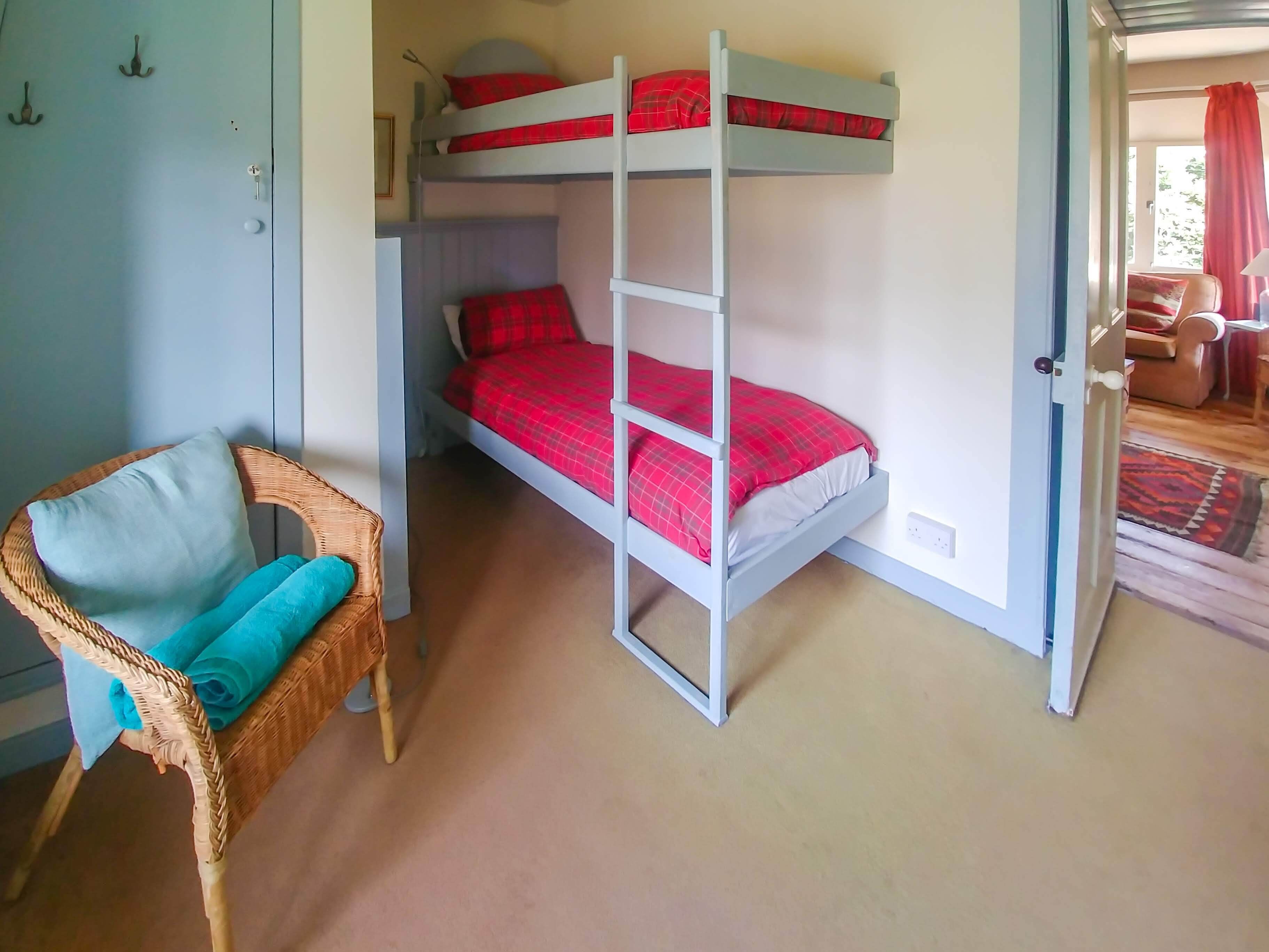 A room with bunk beds, a wicker chair with cushions, and a visible door leading to another room.