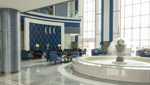 A modern lobby with a central fountain, seating areas, and a patterned wall.