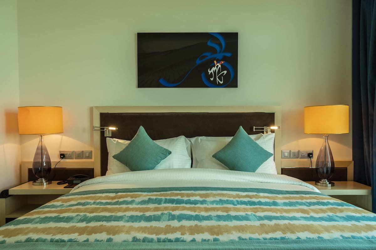 Ein Hotelzimmer mit einem Bett, zwei Nachttischlampen, einem Nachttisch und einem an der Wand befestigten Kunstwerk.