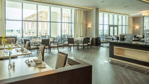 A modern hotel lobby with large windows, a central bar area, and seating arrangements.