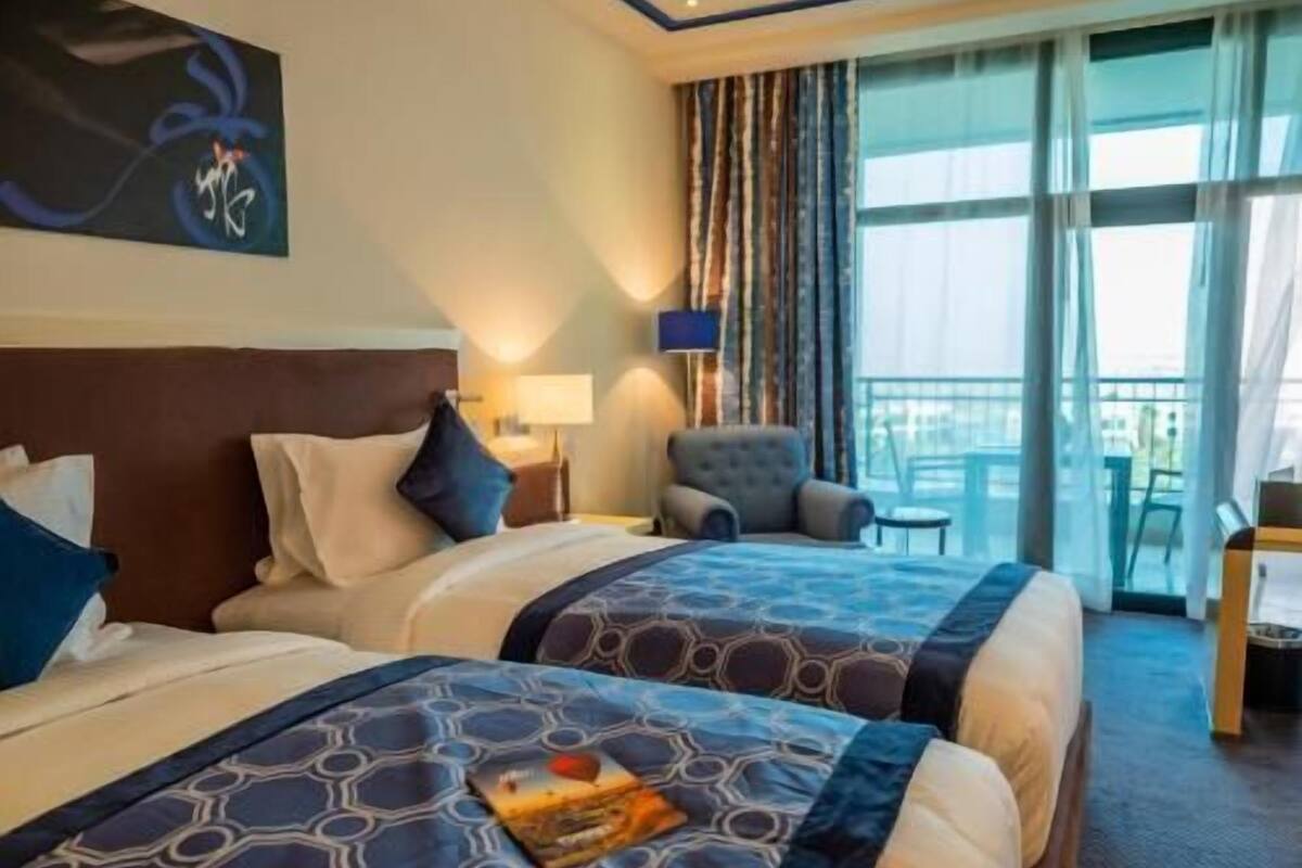 Ein Hotelzimmer mit zwei Betten, einem Sessel, einem Tisch und Blick ins Freie.