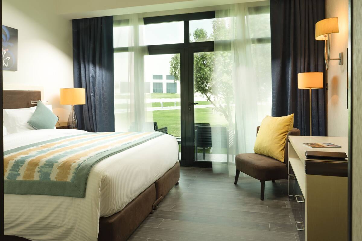 Ein Hotelzimmer mit Bett, Schreibtisch, Stuhl, Lampe und Blick ins Freie.