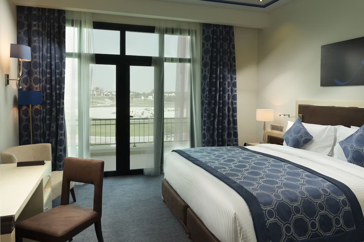 Ein Hotelzimmer mit einem Bett, einem Schreibtisch, einem Sessel und einem großen Fenster mit Vorhängen.