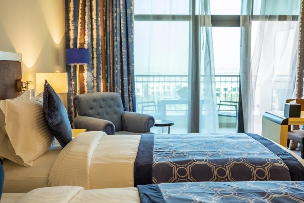 Une chambre d’hôtel avec un grand lit, une chaise, une lampe et une vue sur la ville par la fenêtre.