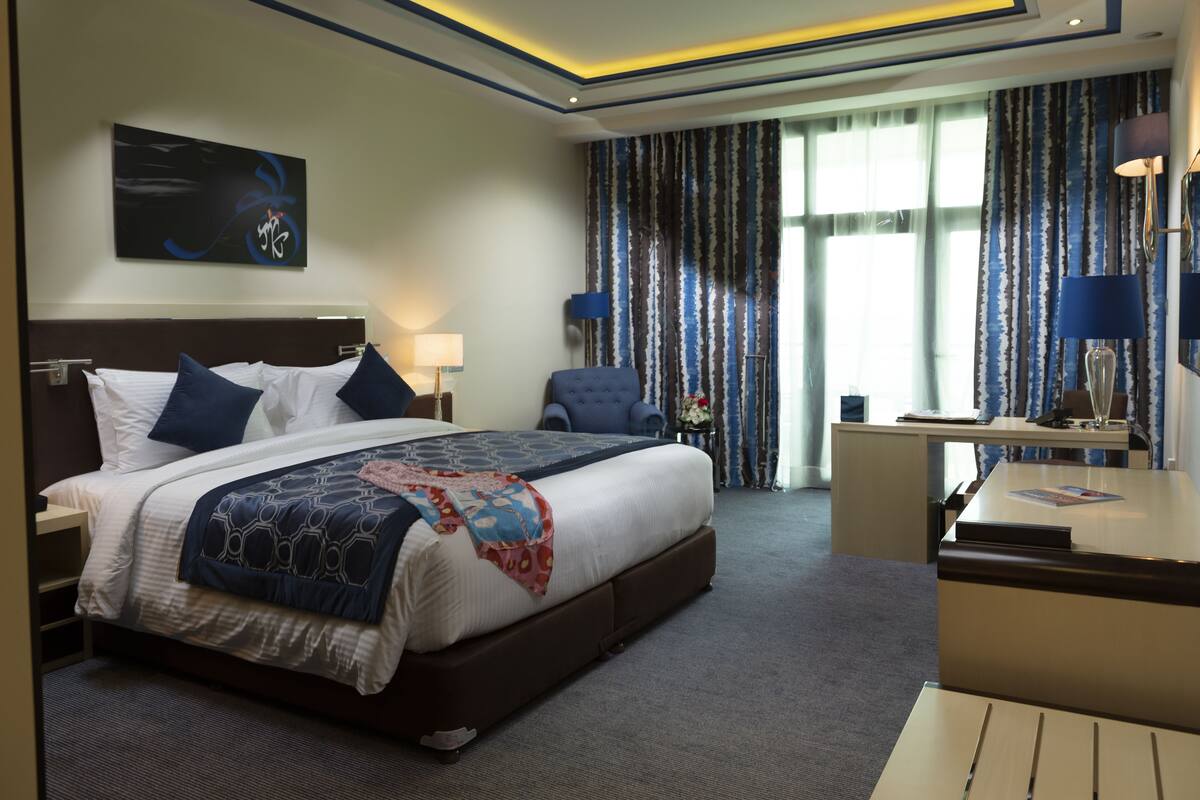 Ein Hotelzimmer mit einem großen Bett, einem Schreibtisch, einem Stuhl, einer Lampe und einem Bild an der Wand.