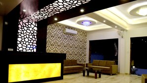 A lobby with a reception desk, two sofas, a coffee table, patterned wallpaper, and a decorative ceiling design. - Hotel Gulmohar Pride (Ahmednagar)