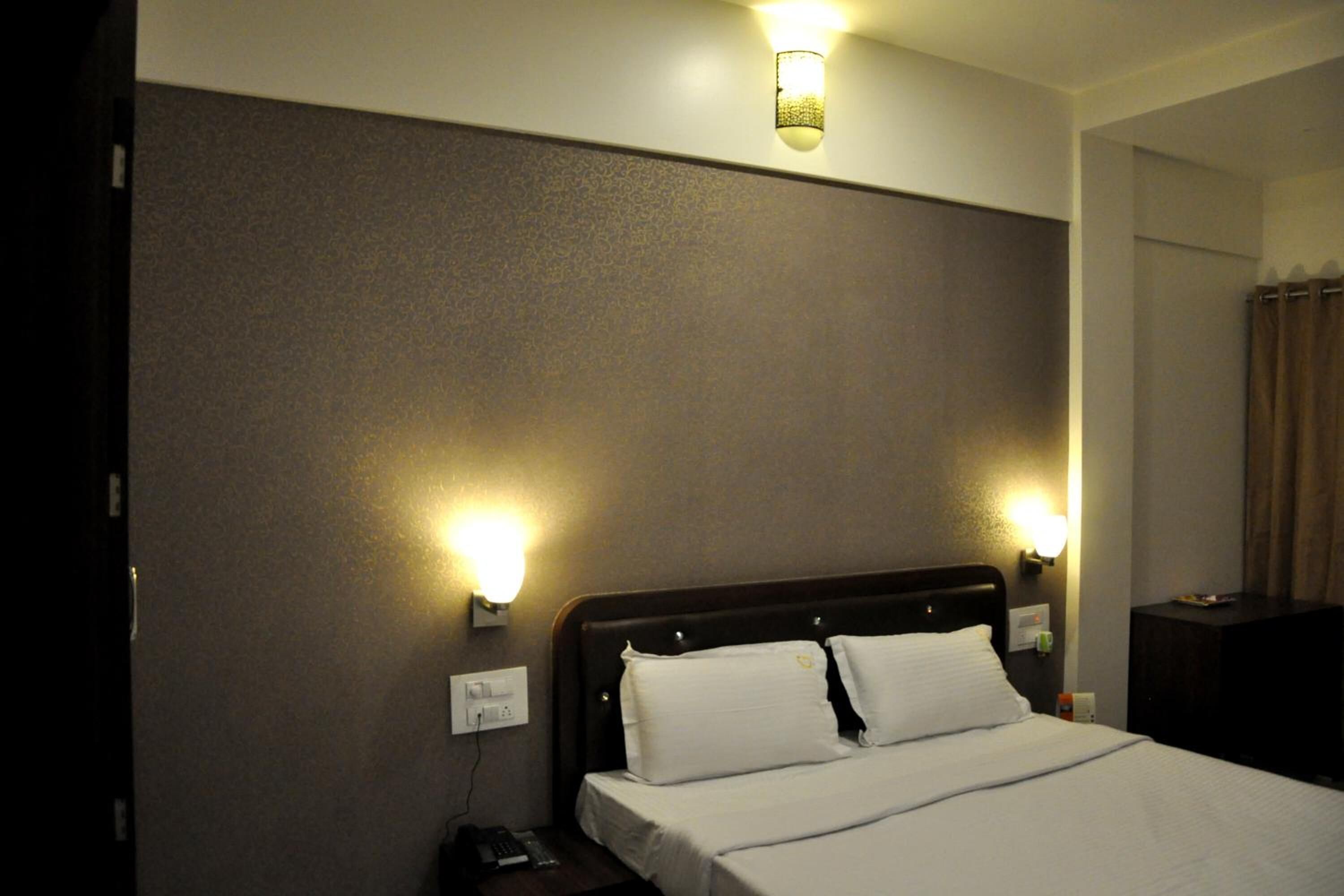 A hotel room with a large bed, two bedside lamps, and a nightstand with a remote control.