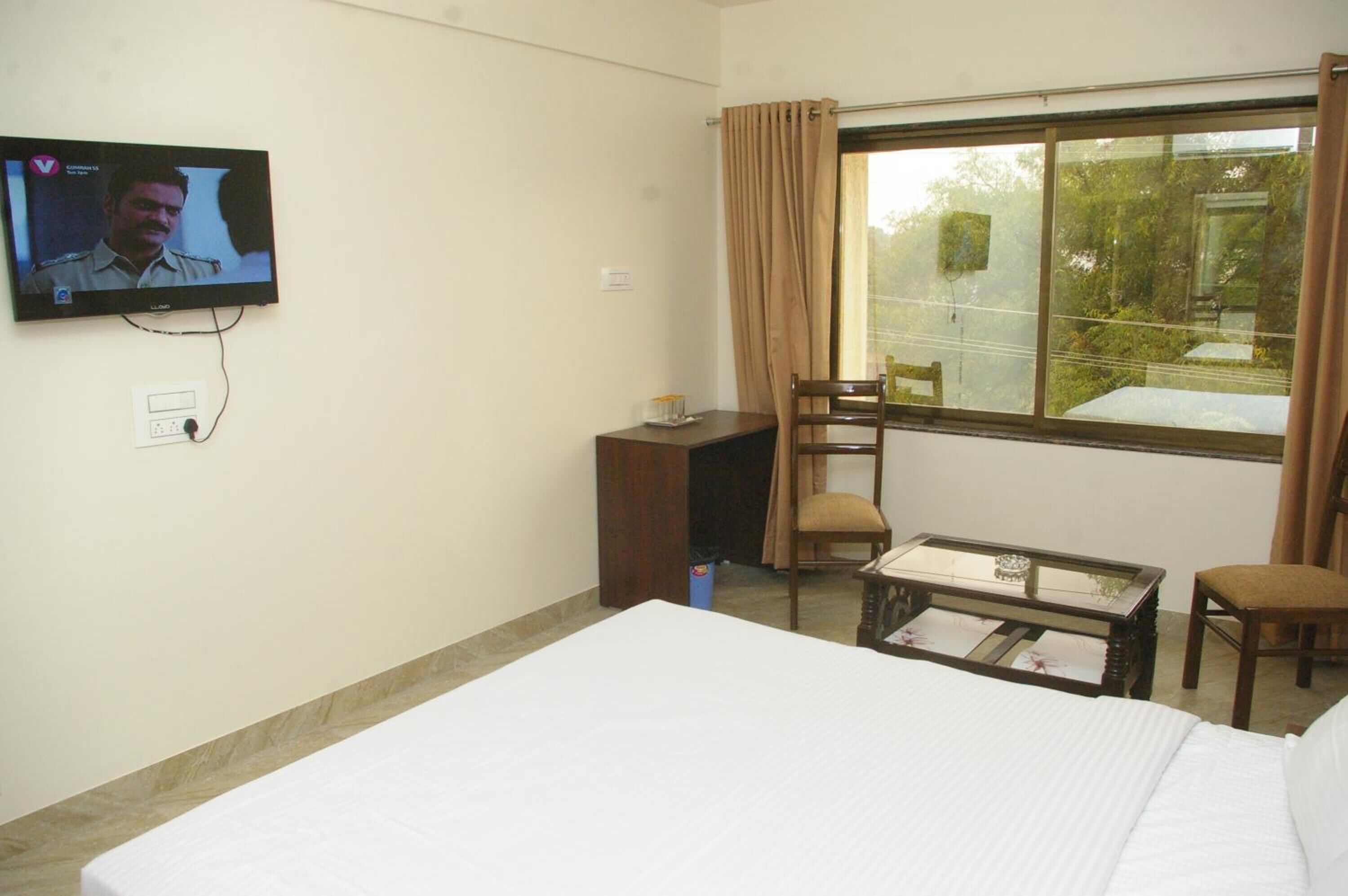 A hotel room with a bed, a desk, a chair, a television, and a window with curtains.