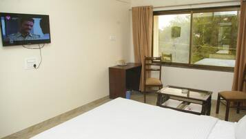 A hotel room with a bed, a desk, a chair, a television, and a window with curtains.