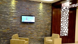 A lobby with a stone wall, a television mounted on it, and two armchairs. - Hotel Gulmohar Pride (Ahmednagar)