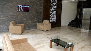 A modern lobby with a brick wall, two beige armchairs, a glass coffee table, and a TV mounted on the wall. - Hotel Gulmohar Pride (Ahmednagar)