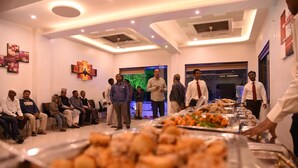 A conference room with a buffet table in the foreground, several people seated and standing, and a modern ceiling design. - Hotel Gulmohar Pride (Ahmednagar)