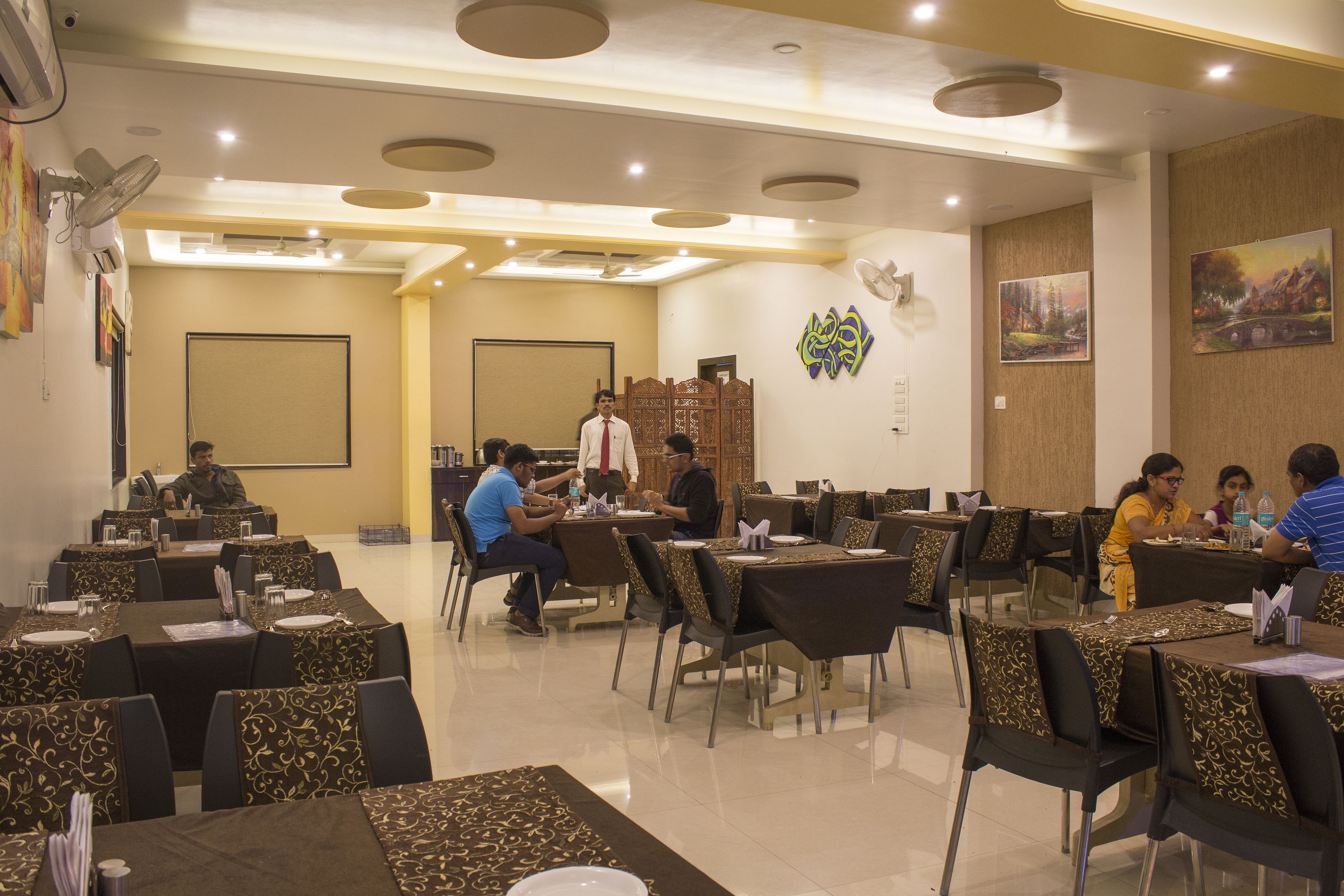 Un restaurante con varias mesas y sillas, un escenario con una persona de pie, y algunos comensales sentados.