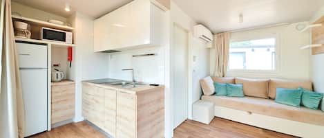 A compact kitchen with a microwave, kettle, and sink, adjacent to a sofa with cushions.