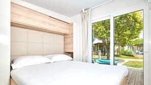 A bedroom with a large bed, wooden headboard, and a view of a garden through a sliding glass door. - Mobile Homes Stella Maris (Umag)