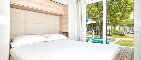 A bedroom with a large bed, wooden headboard, and a view of a garden through a sliding glass door.