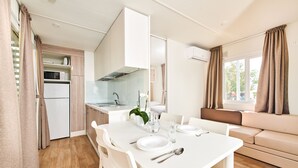 A compact kitchen with a microwave, refrigerator, and a dining area with a table set for two. - Mobile Homes Stella Maris (Umag)