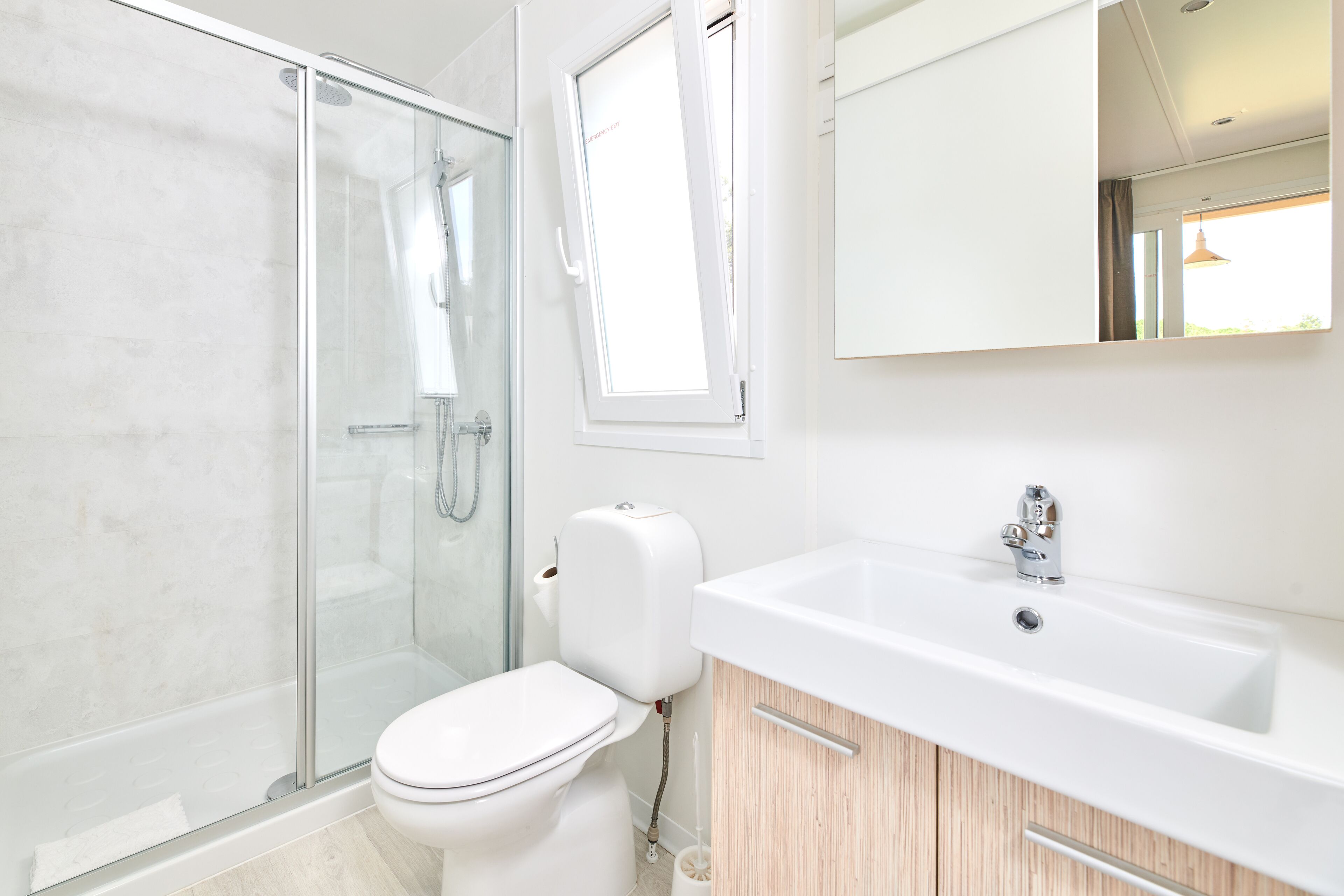A modern bathroom with a glass-enclosed shower, a white toilet, a sink with a mirror, and wooden cabinetry.