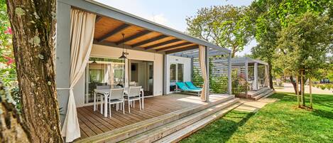 A modern outdoor patio with a wooden deck, a dining area, and a covered seating area.