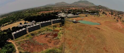 An aerial view of a resort with multiple buildings, a large open field, and a mountain in the background.