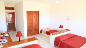 Une chambre avec deux lits simples, un bureau en bois, une lampe rouge et un ventilateur de plafond.