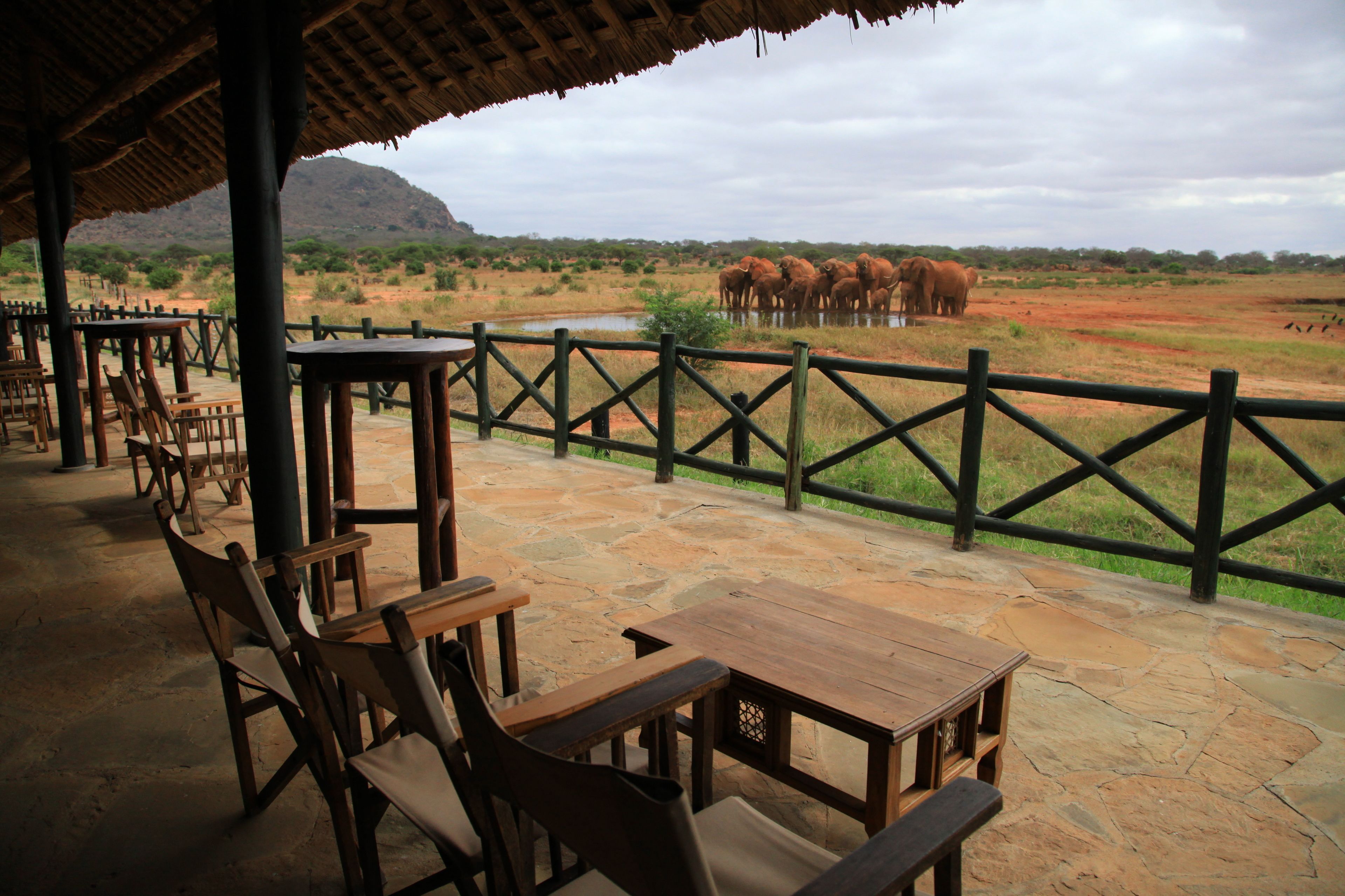 A covered outdoor seating area with stone flooring and wooden tables and chairs.