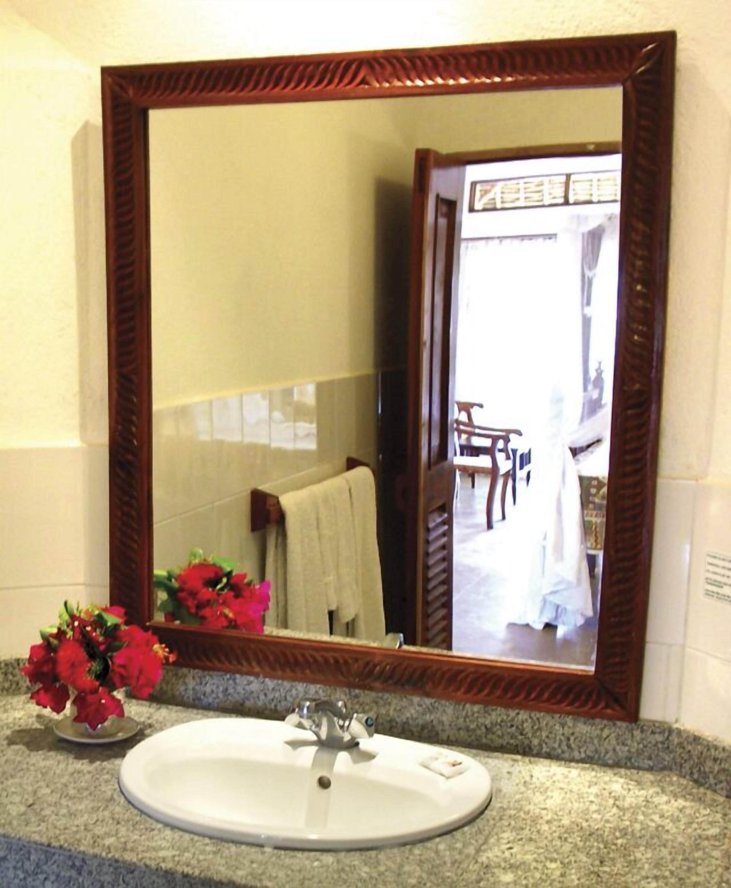 Une salle de bain avec un grand miroir, un lavabo et un vase de fleurs.