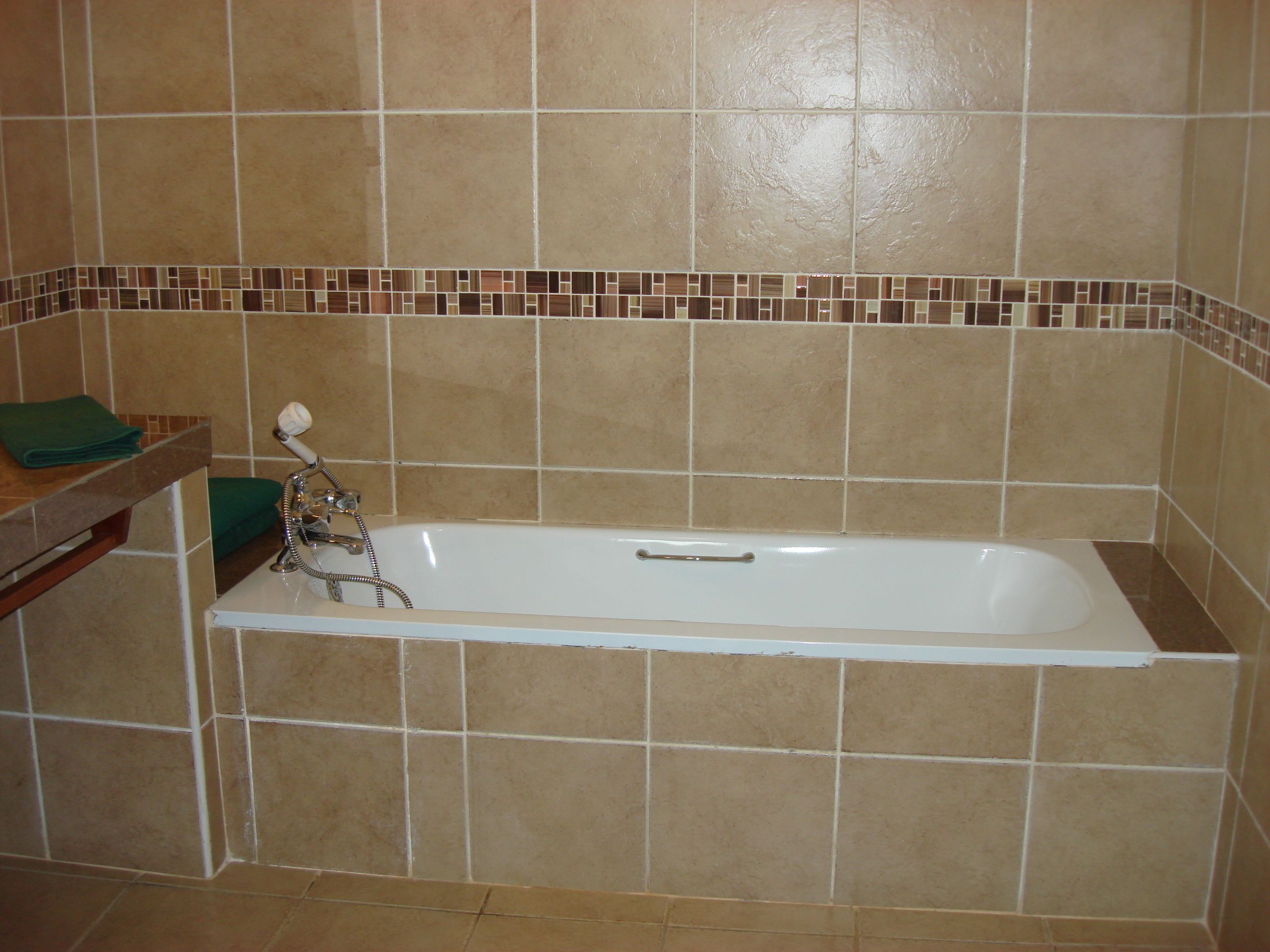 A bathroom with a bathtub, tiled walls, and a green towel on a shelf.