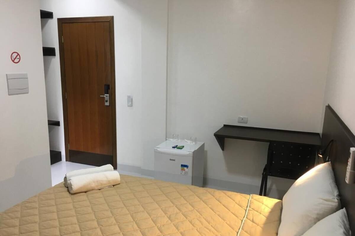 Una habitación de hotel con una cama, un escritorio, una silla, una mesita de noche y una puerta.