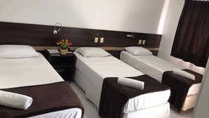 A hotel room with three single beds, a nightstand with a lamp, and a small table with a flower vase. - Executive Hotel (Lucas do Rio Verde)