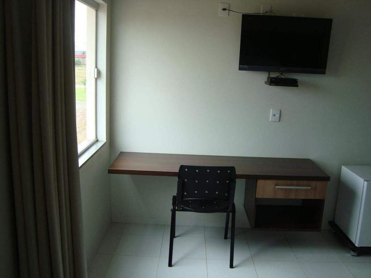 Una habitació amb escriptori, cadira, televisió penjada a la paret i nevera.