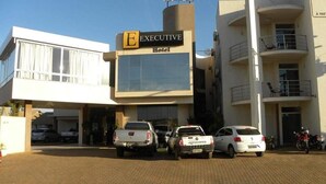A hotel with a sign reading "EXECUTIVE Hotel" and a "HOTEL" sign above it. There are vehicles parked in front, including a white pickup truck and a white sedan. - Executive Hotel (Lucas do Rio Verde)
