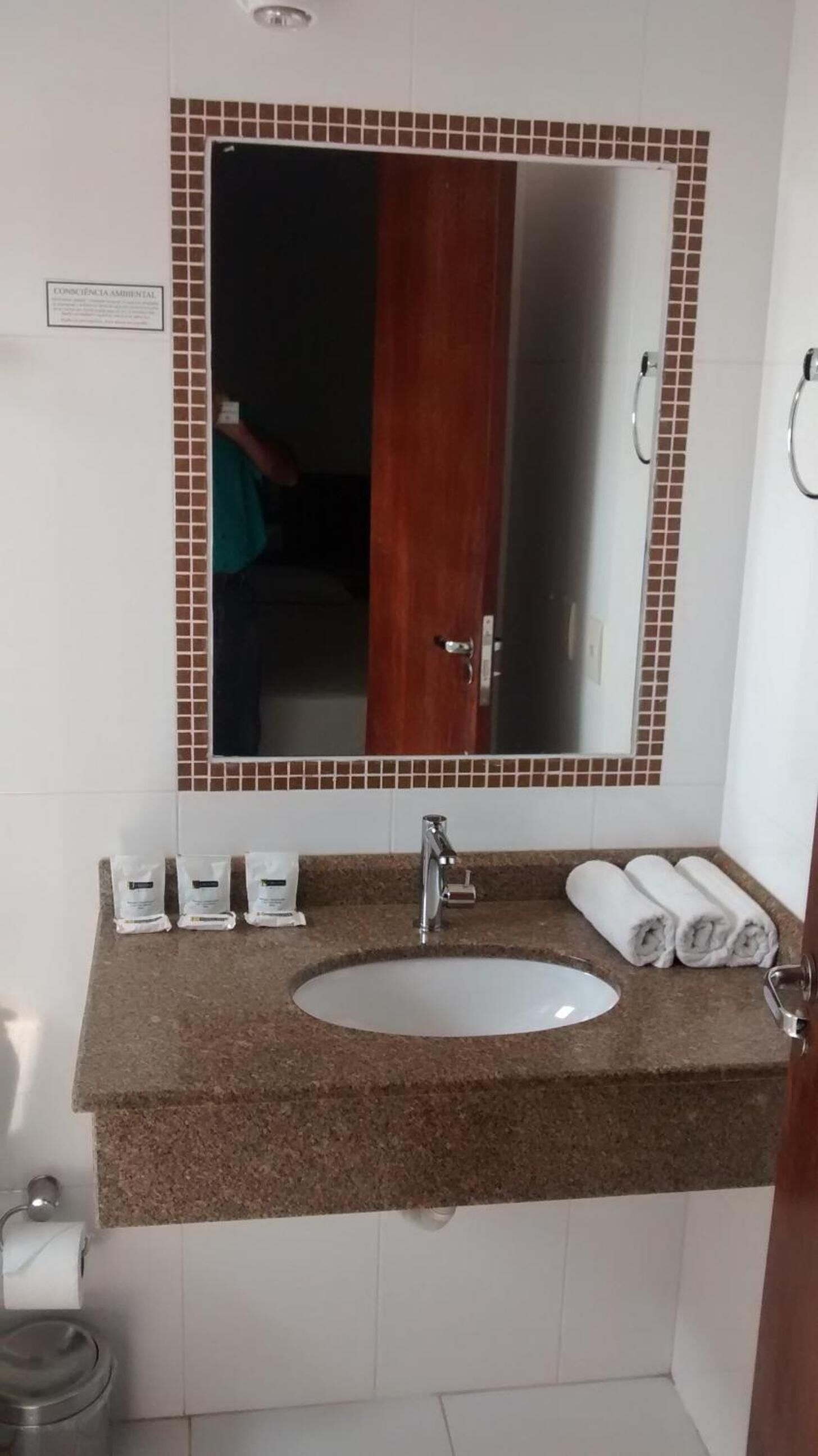 A bathroom with a white sink, a mirror with a brown tile border, and a towel rack with towels.