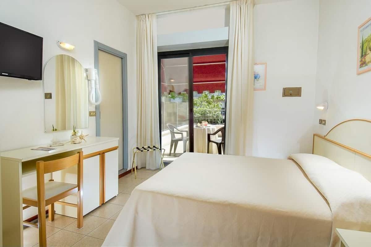 Ein Hotelzimmer mit Bett, Schreibtisch, Stuhl, Fernseher und einem Balkon mit roter Markise.