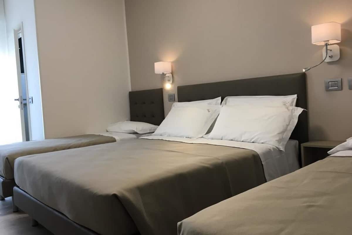 Ein Hotelzimmer mit zwei Betten, einem Kopfteil, Nachttischlampen und einer Tür.