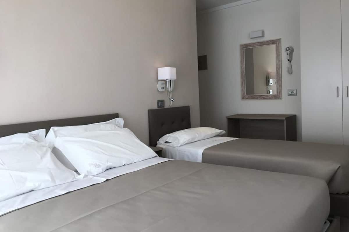 Ein Hotelzimmer mit zwei Betten, einem Nachttisch, einer Lampe, einem Spiegel und einem Kleiderschrank.