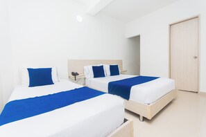 A hotel room with two beds, each with blue and white bedding, a wooden headboard, a bedside table with a phone, and a door to the right. - Hotel Suite Del Parque (Medellín)
