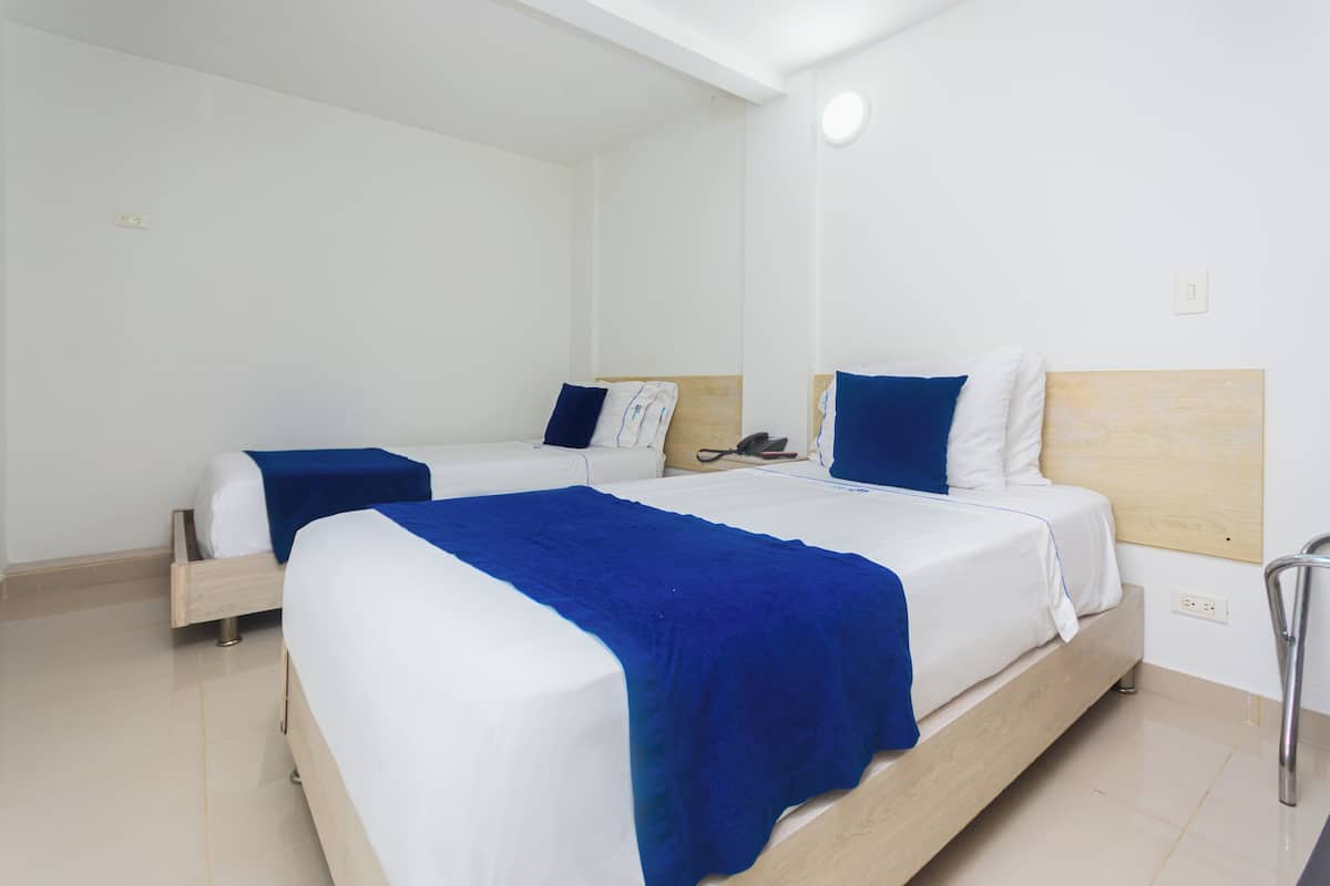 Een hotelkamer met twee bedden, elk voorzien van een houten hoofdbord, witte beddengoed en blauwe plaids.