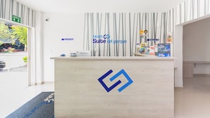 A hotel reception desk with a logo, a reception sign, and a wall with vertical stripes. - Hotel Suite Del Parque (Medellín)
