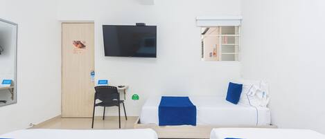 Habitación de hotel con dos camas, un escritorio, una silla, un televisor y una ventana con persianas.