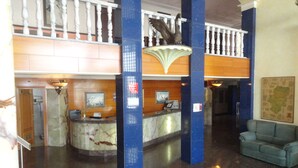 A lobby with a reception desk, a blue and white color scheme, a staircase, and a blue sofa. - Hotel El Cisne (Zaragoza)