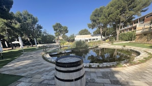 A wooden barrel in a courtyard with a pond, surrounded by stone tiles and greenery. - Hotel El Cisne (Zaragoza)