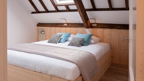 A bedroom with a sloped ceiling, wooden beams, a skylight, a bed with white bedding, patterned pillows, and a wooden floor. - Ruyge Weyde Logies (Oudewater)