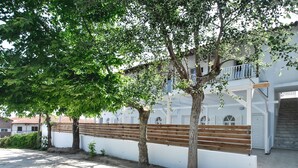A courtyard with a white building, wooden benches, and trees providing shade. - Imeres Studios & Apartments (Kassandra)