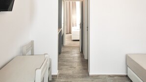 A hallway with a dining table, chairs, a TV mounted on the wall, and an air conditioning unit. - Imeres Studios & Apartments (Kassandra)