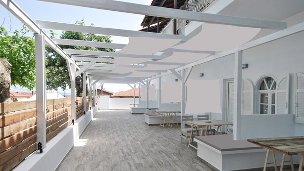 A spacious indoor area with a wooden floor, white walls, and a wooden fence. There are tables and chairs arranged for dining or meetings. - Imeres Studios & Apartments (Kassandra)