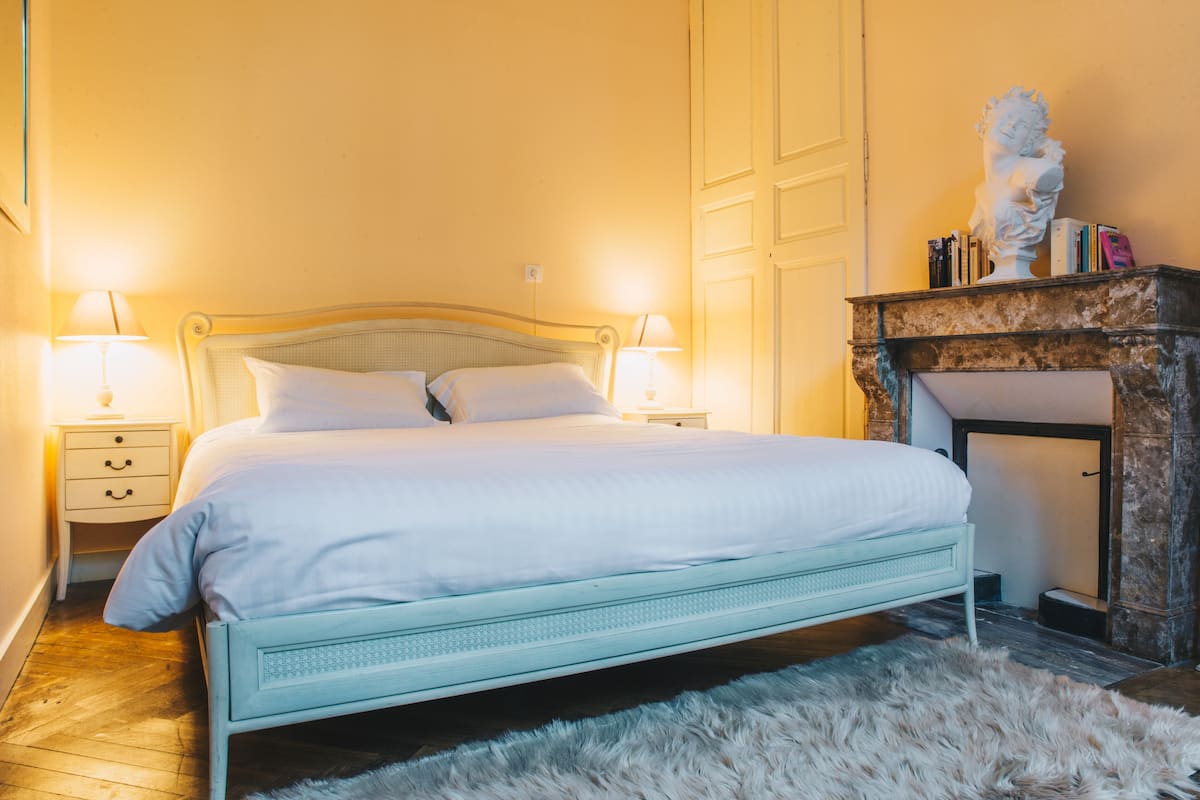 A bedroom with a bed, bedside tables, a lamp, a fireplace, and a statue.