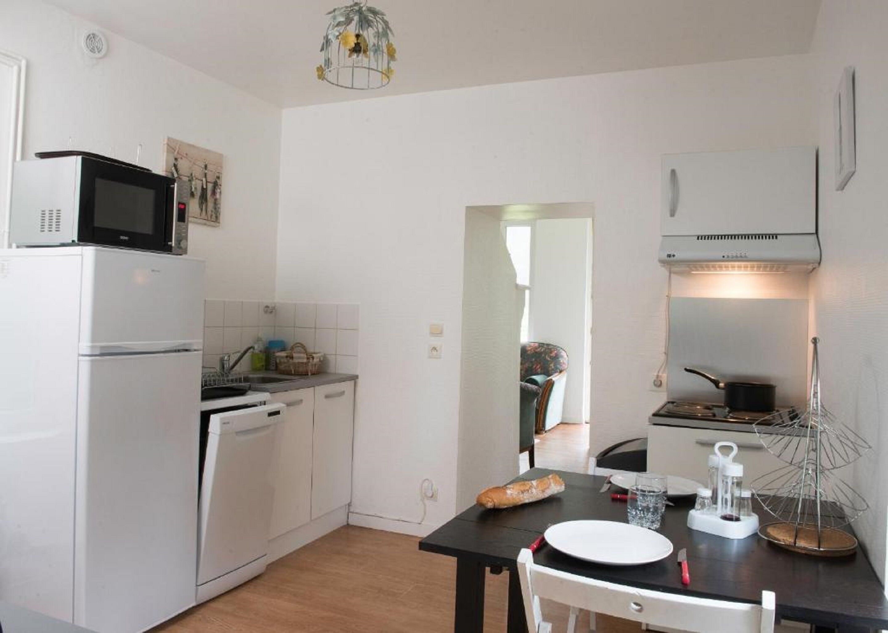 A compact kitchen with a refrigerator, microwave, and stove. There's a dining table with a loaf of bread and a glass of water.