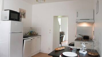 A compact kitchen with a refrigerator, microwave, and stove. There's a dining table with a loaf of bread and a glass of water.